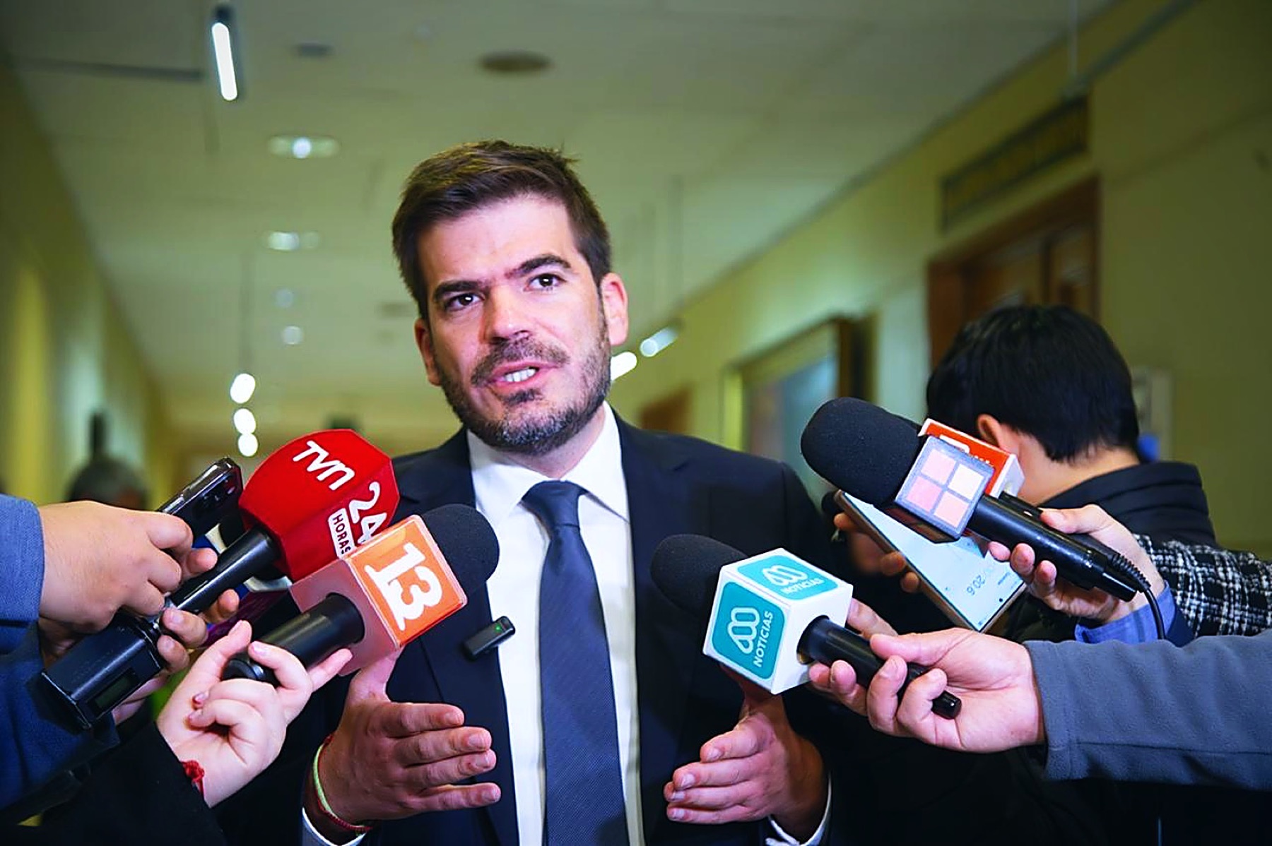 El diputado José Montalva respondiendo preguntas en un punto de prensa, rodeado de micrófonos de canales de televisión
